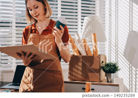 Picture of serious concentrated young Caucasian female artist sitting at desk with painting accessories, holding tube of oil paint, mixing colors on palette; unfinished painting on canvas near her Picture of serious concentrated young Caucasian female artist sitting at desk with painting accessories, holding tube of oil paint, mixing colors on palette; unfinished painting on canvas near her 140235289