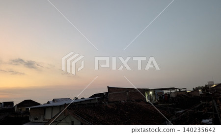 Wide view captures a beautiful sunset sky with orange hues over a dark urban neighborhood silhouette. Traditional rooftop tiles create a beautiful minimalist presentation background template. Wide view captures a beautiful sunset sky with orange hues over a dark urban neighborhood silhouette. Traditional rooftop tiles create a beautiful minimalist presentation background template. 140235642