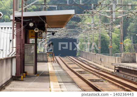 從一座安靜、荒涼的高架車站的月台上,可以看到鐵軌和綠樹成蔭的隧道。 從一座安靜、荒涼的高架車站的月台上,可以看到鐵軌和綠樹成蔭的隧道。 140236443