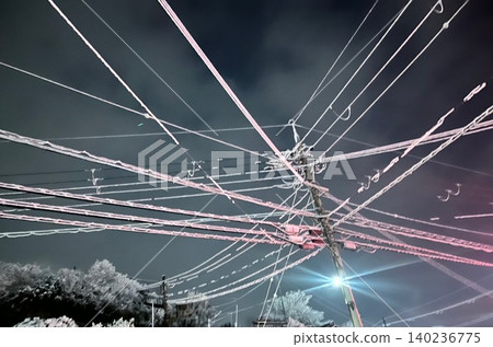 夜幕降臨,無數電線和燈火通明的電線桿縱橫交錯於夜空。 夜幕降臨,無數電線和燈火通明的電線桿縱橫交錯於夜空。 140236775