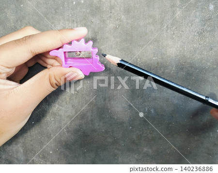 Hand Holding Pencil and Sharpener on Concrete Wall Background Hand Holding Pencil and Sharpener on Concrete Wall Background 140236886