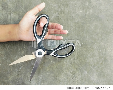 Hand Holding Scissors Against Grey Concrete Wall Background 140236897