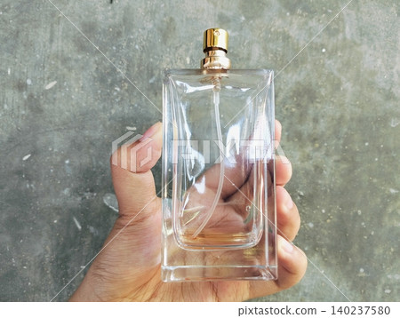 Hand Holding an Empty Perfume Bottle on Concrete Wall Background Hand Holding an Empty Perfume Bottle on Concrete Wall Background 140237580