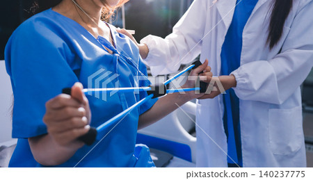 Physical therapist giving stretching exercises with elastic exercise bands and physical therapist hands helping male patient Physical therapy concept Physical therapist giving stretching exercises with elastic exercise bands and physical therapist hands helping male patient Physical therapy concept 140237775