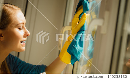 Girl cleaning window at home using detergent rag Girl cleaning window at home using detergent rag 140238180