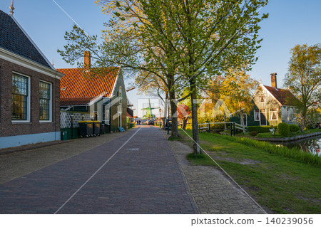 Historic Dutch village with cobblestone street and green windmill under golden sunset light Historic Dutch village with cobblestone street and green windmill under golden sunset light 140239056