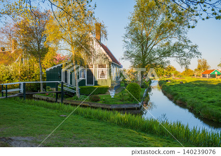 Cozy green Dutch house with wooden bridge along rural canal in golden hour light Cozy green Dutch house with wooden bridge along rural canal in golden hour light 140239076