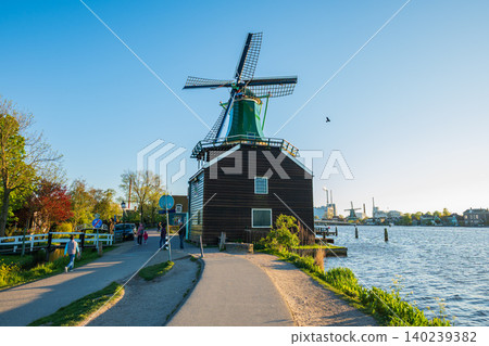 Historic green Dutch windmill on river bank with pedestrian path at sunny sunset 140239382