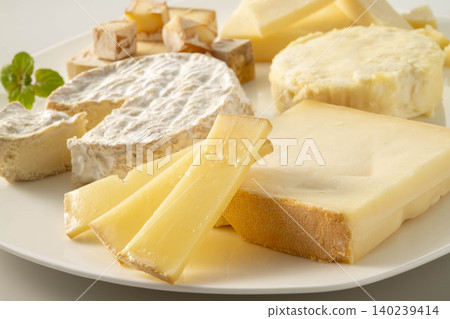 A cheese platter, featuring a selection of white mold cheeses and hard cheeses, served on a cheese board. 140239414