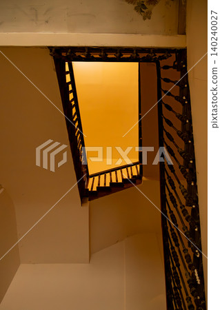 Historic Interior Stairwell Viewed from Below with Ornate Iron Railings and Warm Ambient Light Historic Interior Stairwell Viewed from Below with Ornate Iron Railings and Warm Ambient Light 140240027