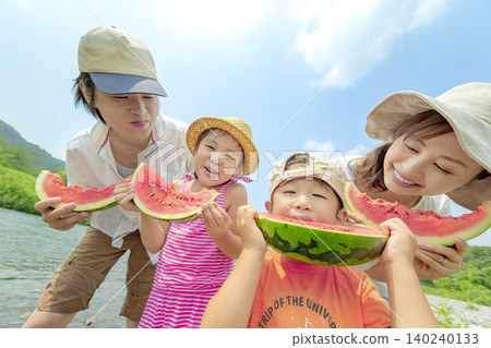 A family of four eating watermelon by the river in summer. A family of four eating watermelon by the river in summer. 140240133