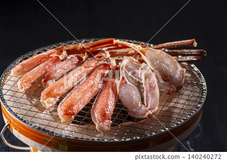 Grilling snow crab over charcoal in a shichirin (small charcoal grill) - Luxurious seafood grill against a black background. Grilling snow crab over charcoal in a shichirin (small charcoal grill) - Luxurious seafood grill against a black background. 140240272