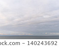 The lingering glow of a delicate sunrise shimmering beneath a cloudy sky, and the calm sea. 140243692