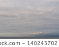 Beneath the gray clouds, the pastel horizon shimmers and the sea is calm. 140243702