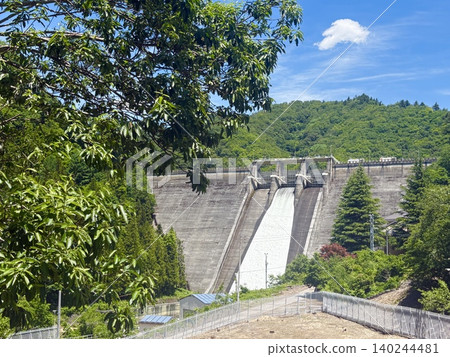 The magnificent sight of water being released from the Sudagai Dam, set against the summer sky and lush greenery. The magnificent sight of water being released from the Sudagai Dam, set against the summer sky and lush greenery. 140244481