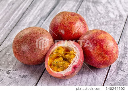 Fresh passion fruit with cut open one revealing juicy seeds on rustic wooden surface 140244602