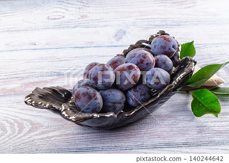 Fresh ripe purple plums in black ceramic bowl on wooden table Fresh ripe purple plums in black ceramic bowl on wooden table 140244642