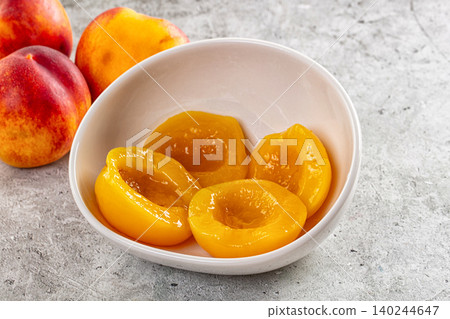 canned peach halves in white bowl with fresh peaches on stone surface canned peach halves in white bowl with fresh peaches on stone surface 140244647