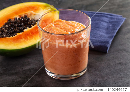 Fresh papaya smoothie in glass with half papaya fruit on dark table 140244657