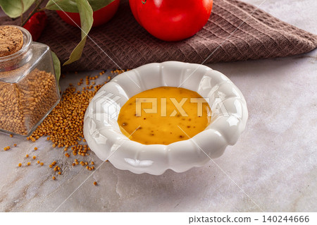 Yellow mustard sauce in white ceramic bowl with mustard seeds and tomatoes Yellow mustard sauce in white ceramic bowl with mustard seeds and tomatoes 140244666