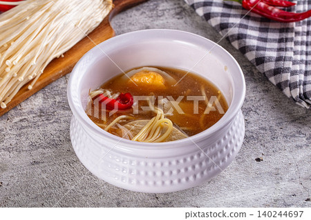 Hot noodle soup with enoki mushrooms, chili peppers, and tofu in white bowl on rustic table Hot noodle soup with enoki mushrooms, chili peppers, and tofu in white bowl on rustic table 140244697