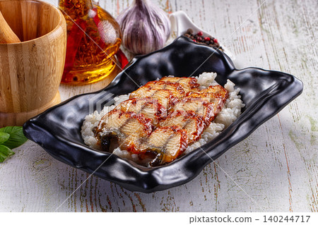 Grilled eel unagi served on white rice in black ceramic bowl with garlic and oil Grilled eel unagi served on white rice in black ceramic bowl with garlic and oil 140244717