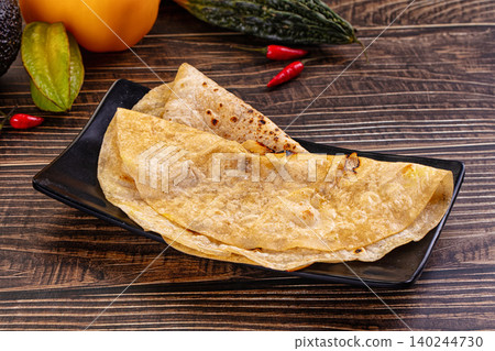 Crispy golden pancakes with charred spots on a black rectangular plate, surrounded by fresh vegetables on a wooden table Crispy golden pancakes with charred spots on a black rectangular plate, surrounded by fresh vegetables on a wooden table 140244730