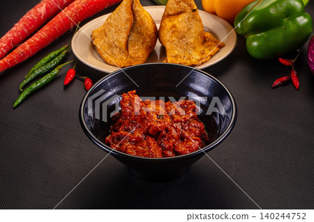 Spicy red curry in black bowl with samosas and fresh vegetables Spicy red curry in black bowl with samosas and fresh vegetables 140244752