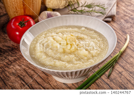 Homemade cauliflower cream soup with fresh ingredients like tomato, garlic, and rosemary on a rustic wooden background Homemade cauliflower cream soup with fresh ingredients like tomato, garlic, and rosemary on a rustic wooden background 140244767