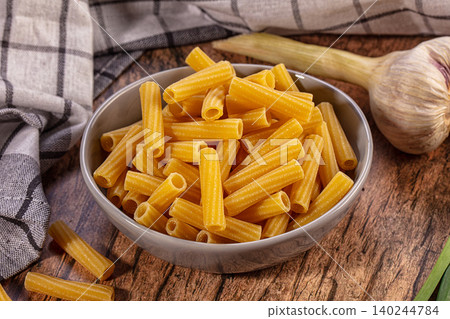 Raw ziti pasta in ceramic bowl with garlic and checkered cloth on wooden table Raw ziti pasta in ceramic bowl with garlic and checkered cloth on wooden table 140244784