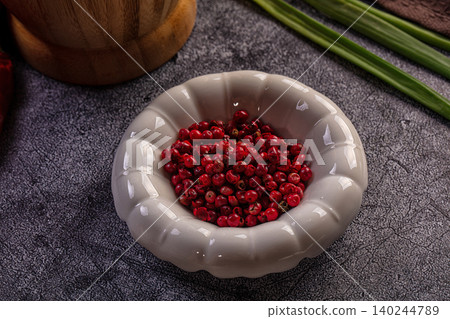 Pink peppercorns in ceramic bowl on dark stone surface Pink peppercorns in ceramic bowl on dark stone surface 140244789