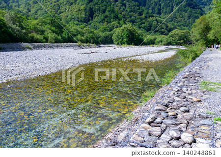 在夏日的陽光下,上高地梓川清澈見底的河水和鬱鬱蔥蔥的青山閃閃發光。 在夏日的陽光下,上高地梓川清澈見底的河水和鬱鬱蔥蔥的青山閃閃發光。 140248861