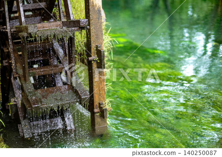 一座風景如畫的木製水車在清澈見底的溪流中轉動，濺起陣陣水花。 140250087