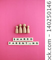 Wooden family figures discussing shared parenting on pink background 140250146