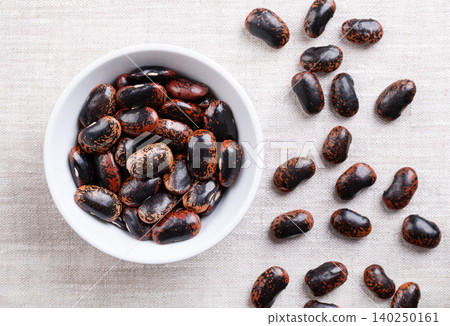 Scarlet Runner beans in a white bowl on linen fabric. Dried, raw seeds of large and speckled runner beans, a variety of Phaseolus coccineus, also known as multiflora bean, butter, or fire bean. Photo Scarlet Runner beans in a white bowl on linen fabric. Dried, raw seeds of large and speckled runner beans, a variety of Phaseolus coccineus, also known as multiflora bean, butter, or fire bean. Photo 140250161