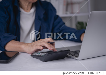 Close up senior woman hand using calculator and holding pen. Elderly lady calculating retirement pension, healthcare insurance budget, and paying bills online with laptop at home. Close up senior woman hand using calculator and holding pen. Elderly lady calculating retirement pension, healthcare insurance budget, and paying bills online with laptop at home. 140250719