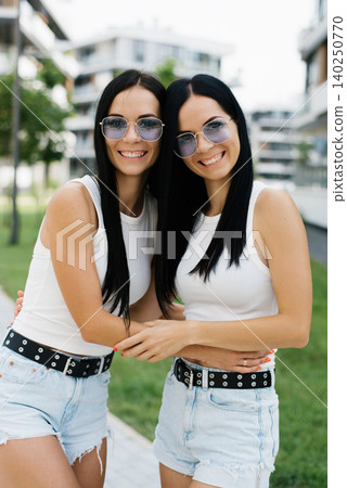 Customer Twin Sisters Smiling and Hugging Outdoors Customer Twin Sisters Smiling and Hugging Outdoors 140250770
