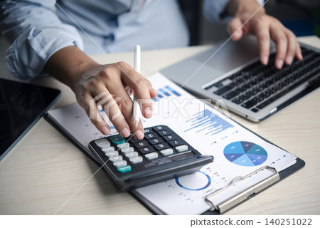 Calculator, finance Analyst presses calculator on budget report with charts laptop in office, reviewing data, accounting, numbers, analysis, planning, costs, and profit for decisions. 140251022