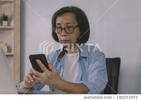 Close up of senior woman hands using smartphone for two-factor authentication while working on laptop. Elderly digital multitasking, mobile banking, and cyber security concept. Close up of senior woman hands using smartphone for two-factor authentication while working on laptop. Elderly digital multitasking, mobile banking, and cyber security concept. 140251072