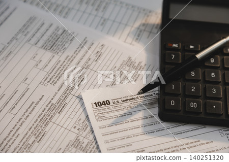 Calculator and pen placed on individual income tax forms and financial documents for calculating taxes, accounting review, payment preparation, expense reporting, and tax filing workflow. Calculator and pen placed on individual income tax forms and financial documents for calculating taxes, accounting review, payment preparation, expense reporting, and tax filing workflow. 140251320