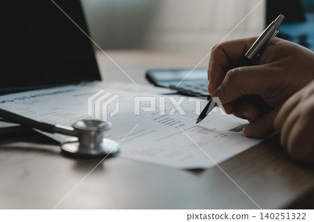 Healthcare professional reviewing a medical billing document with a pen beside a stethoscope and laptop, illustrating insurance claims verification, healthcare reimbursement and medical expense Healthcare professional reviewing a medical billing document with a pen beside a stethoscope and laptop, illustrating insurance claims verification, healthcare reimbursement and medical expense 140251322