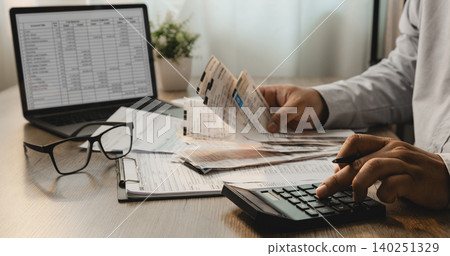 Person reviewing personal income tax forms and receipts while using calculator beside laptop for expense tracking, accounting analysis, tax filing, and financial reporting workflow. Person reviewing personal income tax forms and receipts while using calculator beside laptop for expense tracking, accounting analysis, tax filing, and financial reporting workflow. 140251329