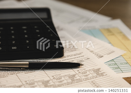 Calculator and pen placed on tax forms and financial statement documents for real estate information, accounting analysis, tax calculation, and financial reporting workflow. Calculator and pen placed on tax forms and financial statement documents for real estate information, accounting analysis, tax calculation, and financial reporting workflow. 140251331