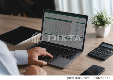Person reviewing data and graphs in spreadsheet documents on a laptop with a calculator, illustrating business analysis, financial reporting, performance tracking and data management workflow. 140251338