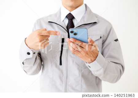 A middle-aged businessman in gray work clothes points to his smartphone against a white background. A middle-aged businessman in gray work clothes points to his smartphone against a white background. 140251963