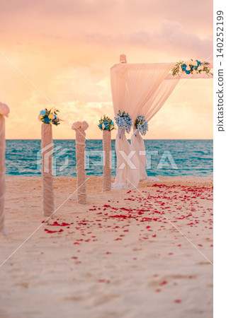 Romantic beach wedding altar draped in white fabric with rose petals lining the sand. Vertical destination ceremony facing the calm tropical sea. Dreamy seaside celebration awaiting the perfect vows. Romantic beach wedding altar draped in white fabric with rose petals lining the sand. Vertical destination ceremony facing the calm tropical sea. Dreamy seaside celebration awaiting the perfect vows. 140252199