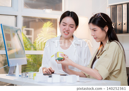 Two asian woman graphic designers analyzing product package prototype, reviewing paper sketch. Two asian woman graphic designers analyzing product package prototype, reviewing paper sketch. 140252361