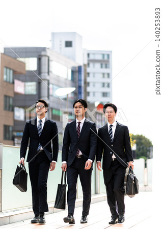 Three men in suits are walking outdoors. Three men in suits are walking outdoors. 140253893