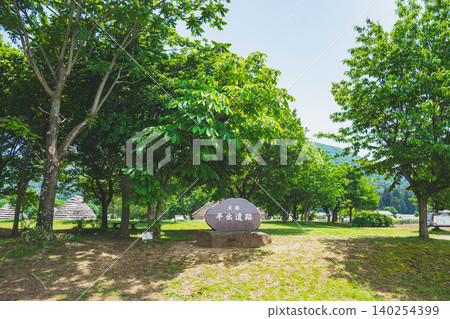 A stone monument and a reconstructed pit dwelling at the Hiraide archaeological site in the fresh greenery. A stone monument and a reconstructed pit dwelling at the Hiraide archaeological site in the fresh greenery. 140254399