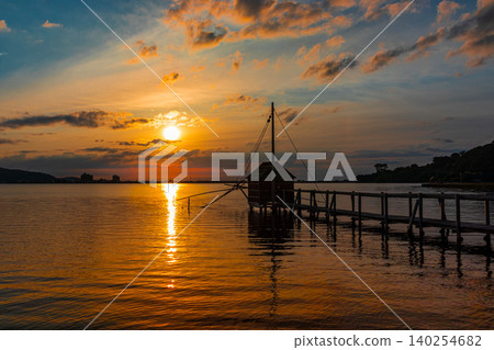 A landscape featuring a lake bathed in the sunset and a watchtower for net fishing. 140254682